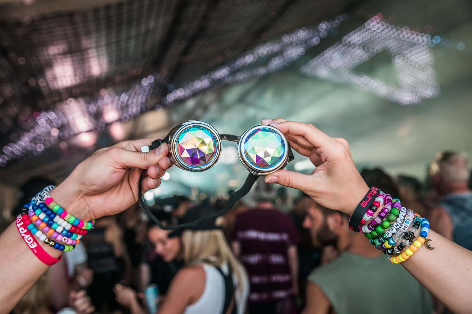 Concert-going couple with festival wristbands holding a pair of prismatic sunglasses.