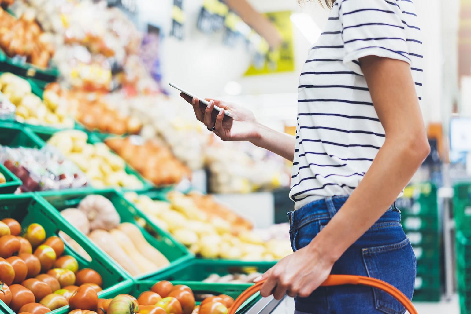 Young woman using smart phone in supermarket to shop for healthy food.