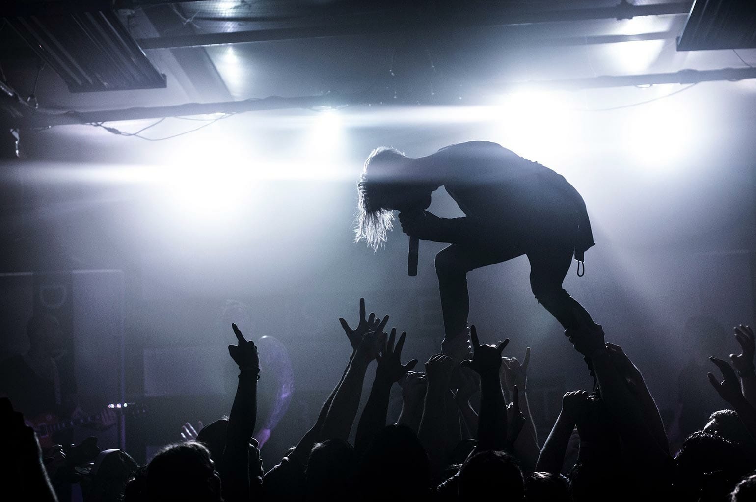 A crowd of concert goers cheering a singer on in a club.