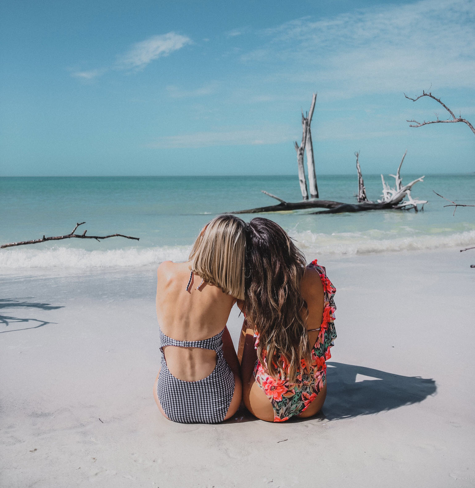 Brunette and blonde bloggers sitting on the sand together staring out into the ocean