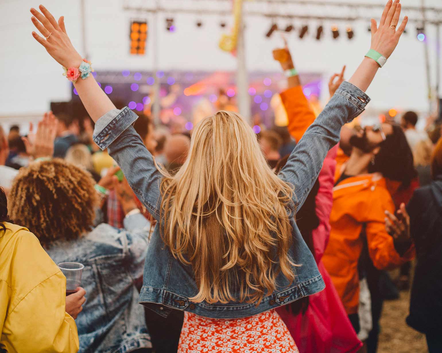 Young girl standing in a crowd at a music festival looking towards the stage.