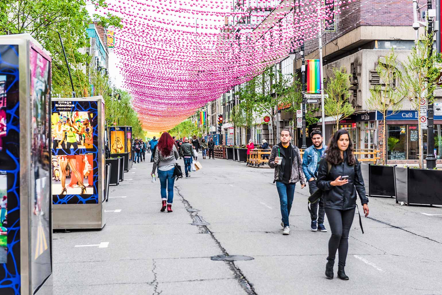 People strolling down the street in Montreal with colorful decorations hanging above and around them.