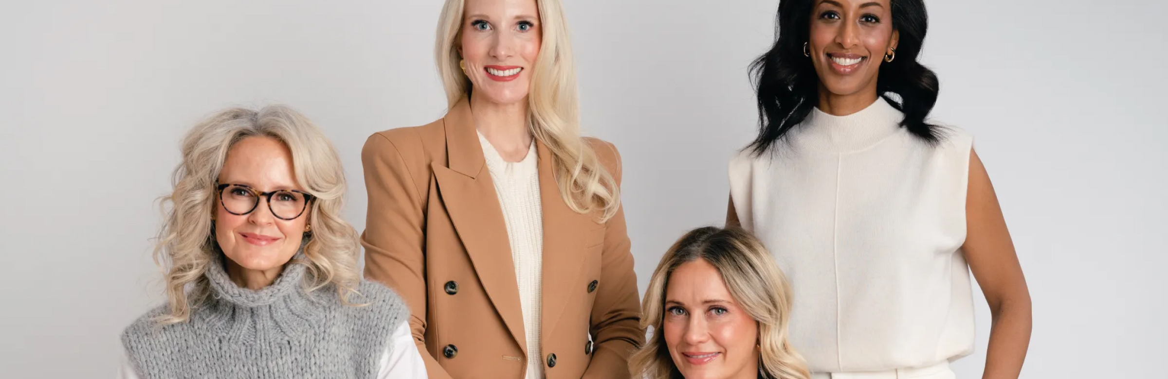 Four women in professional business attire pose together against a neutral background