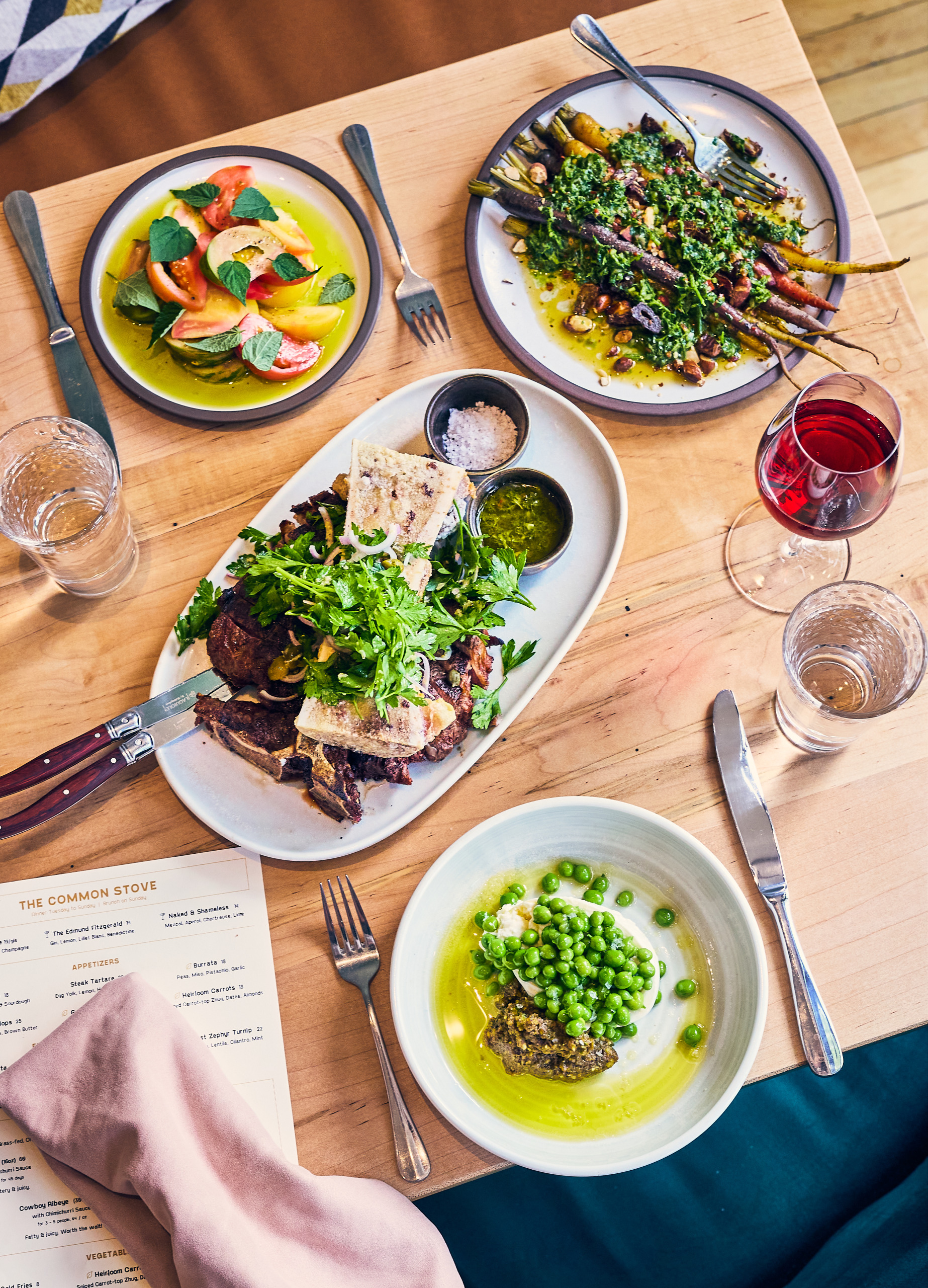 A full dinner table with peas, carrots, asparagus and steaks 