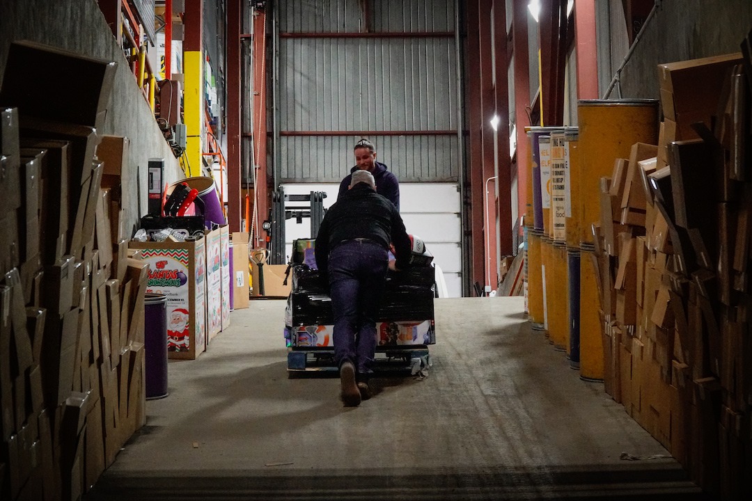 Two volunteers push a trolly loaded with food up a ramp inside the Regina Food Bank