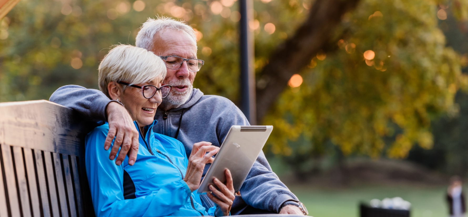 A couple sitting on a bench and looking at an iPad. 