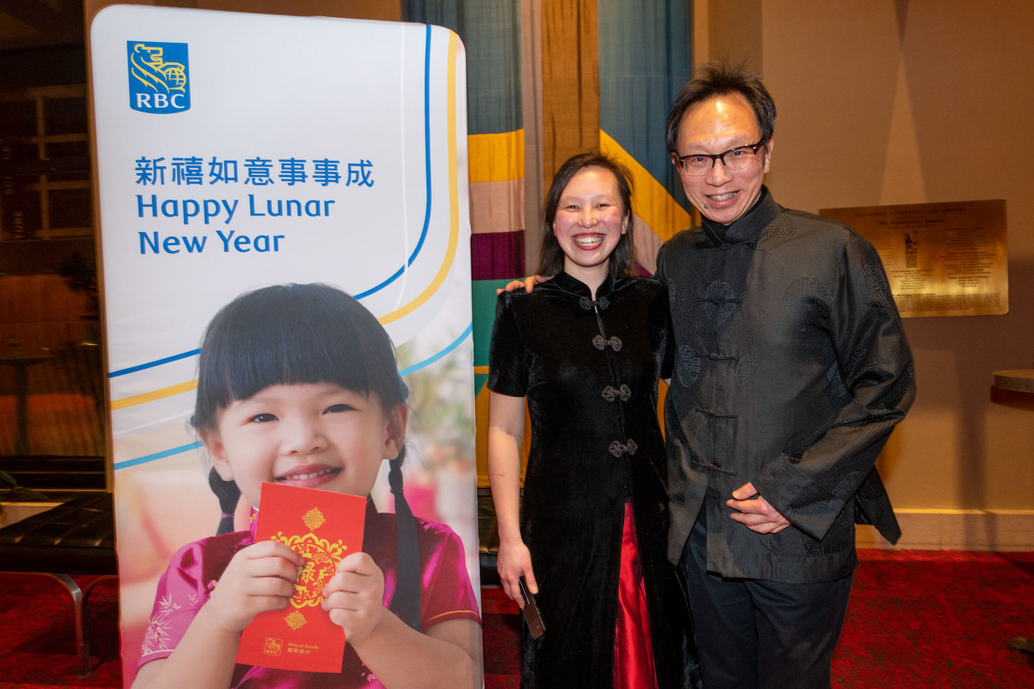 Conductor Naomi Woo and her father smiling beside a banner for a Lunar New Year concert sponsored by RBC