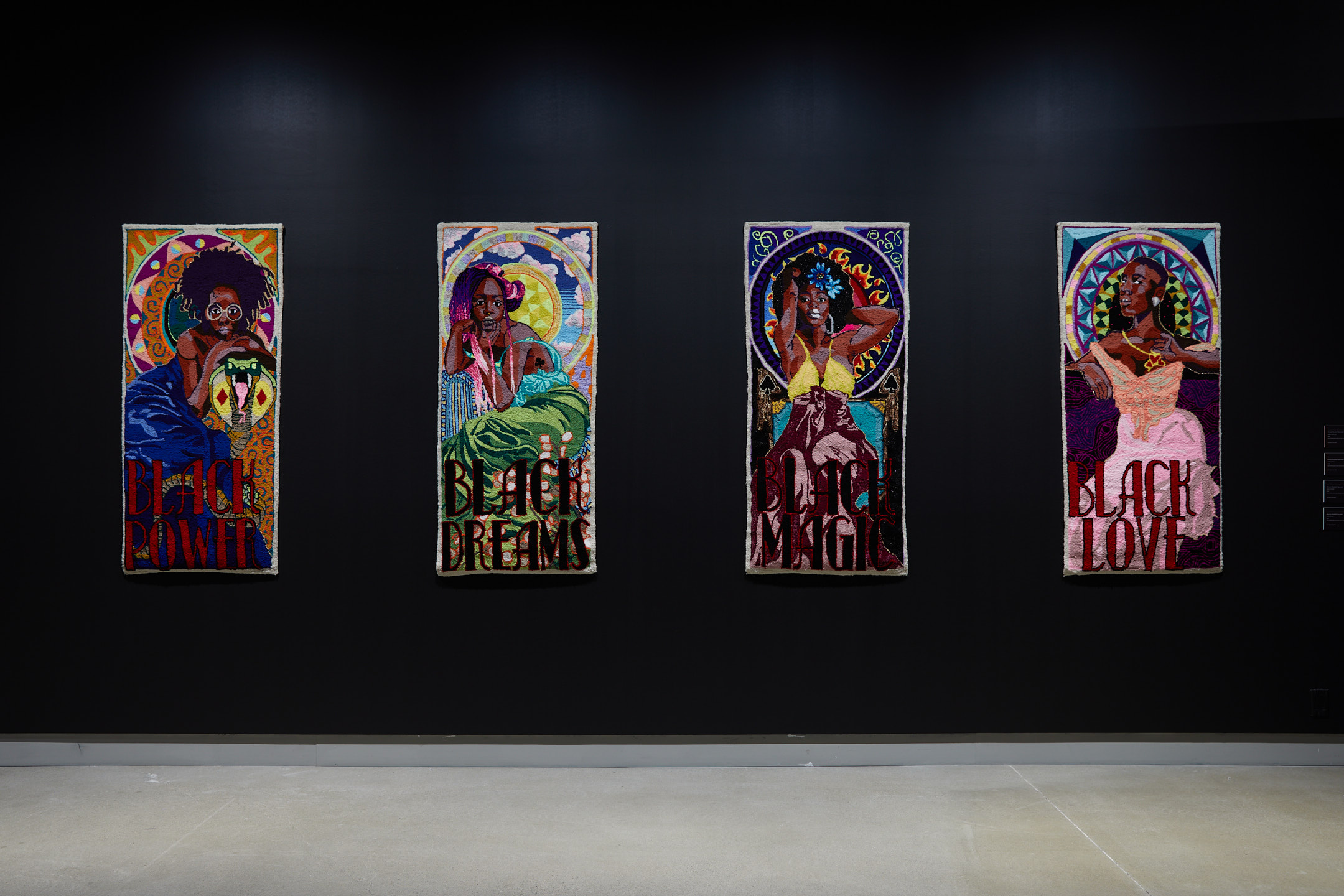Four tapestries hang side-by-side in an exhibit, each featuring a black woman.