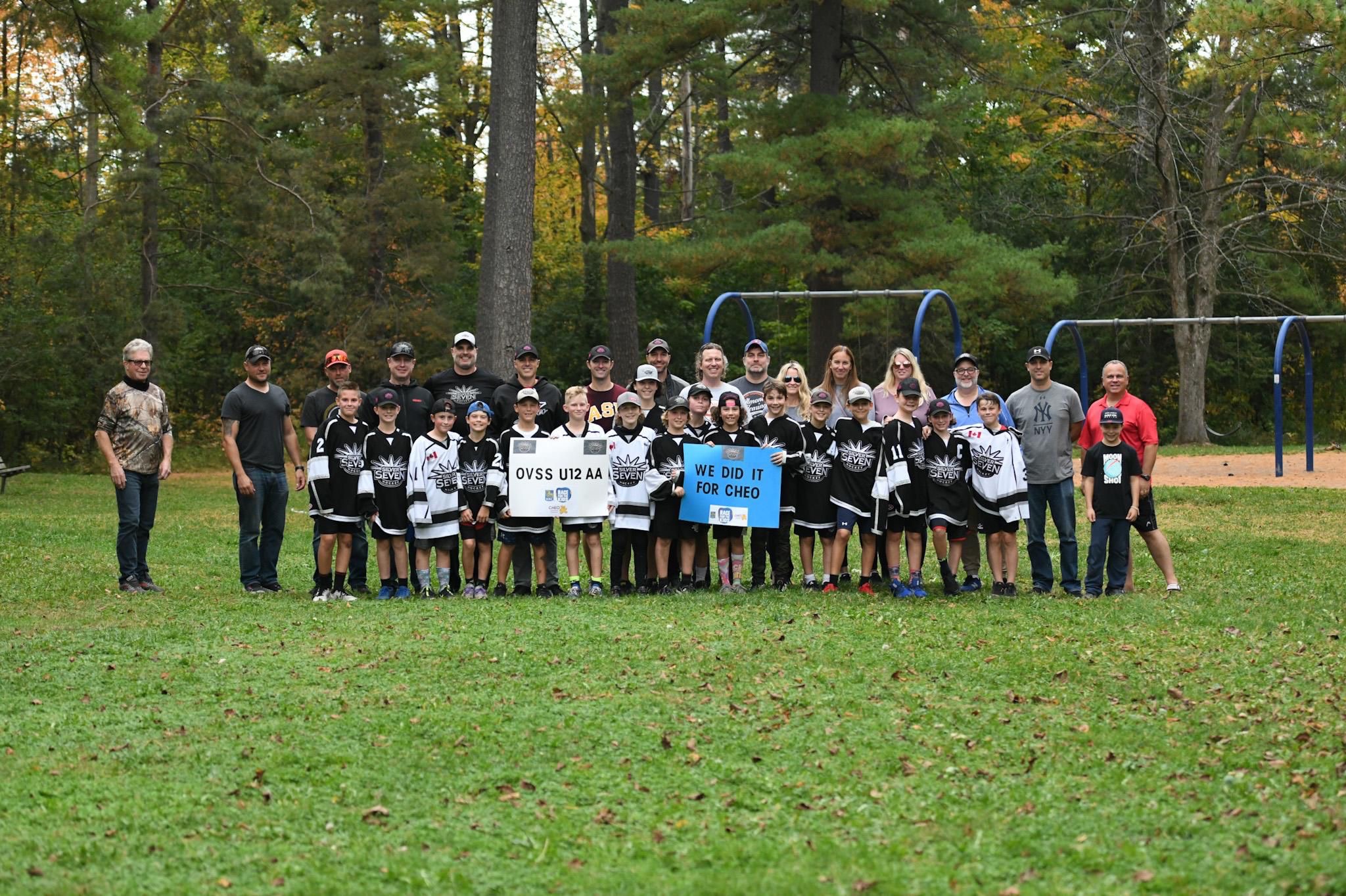 The Silver Sevens U12AA hockey team and coaches on a field, holding the signs 