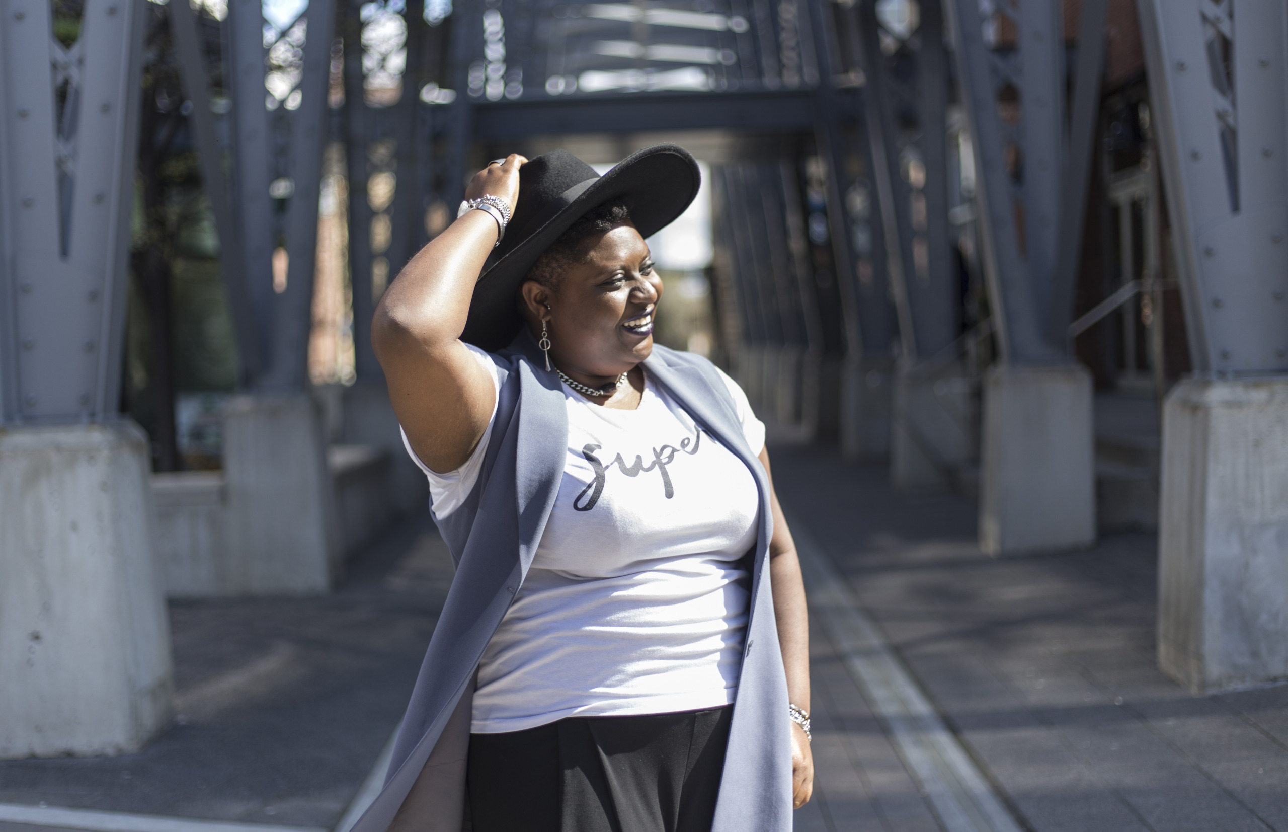Tyler Ferguson, founder of Monoxide standing on a bridge, holding her hat, smiling with 