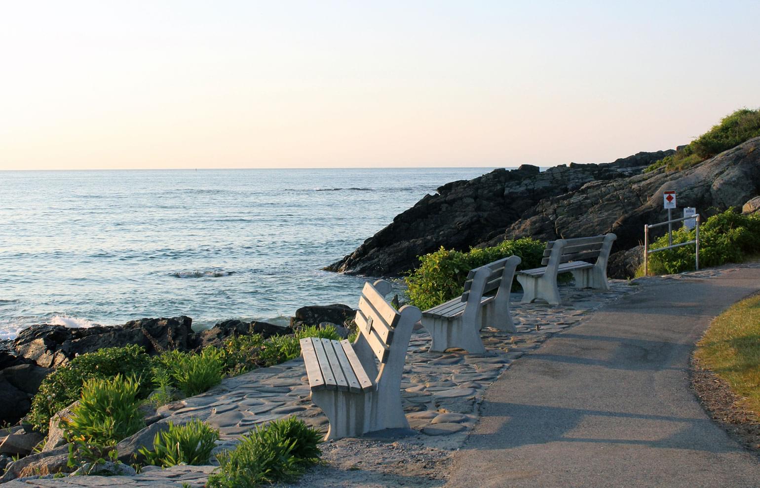 Park benches overlook the shore at sunset in Ogunquit, Maine.