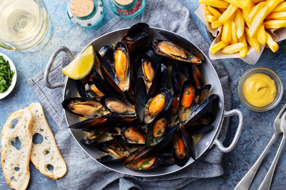 Mussels with lemon slice in cooking pan with French fries on the side and two slices of baguette.