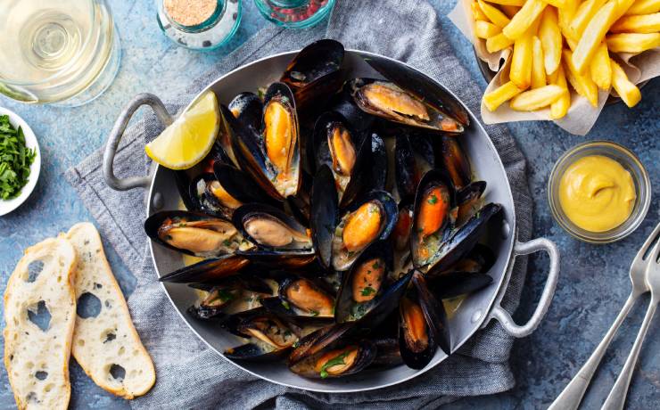 Mussels with lemon slice in cooking pan with French fries on the side and two slices of baguette.