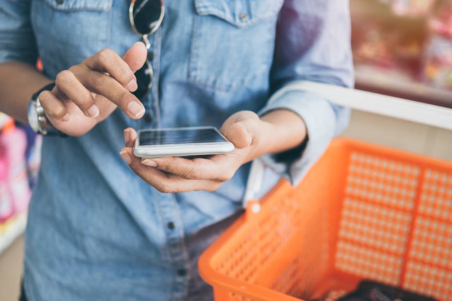 Woman in denim shirt looks on her phone at a grocery store