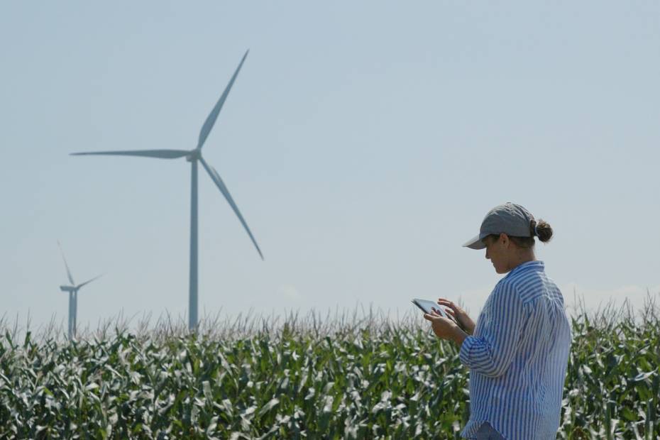 A female ESG inspector working on a tablet in a field with a windmill in the background