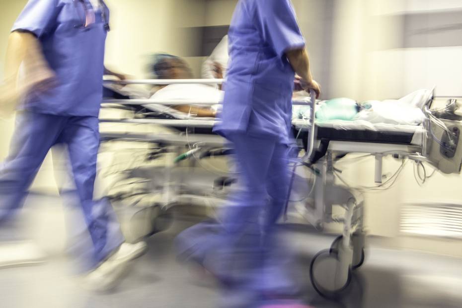 A blurred image showing a doctor and a nurse pulling hospital trolley quickly along the hospital hallway.