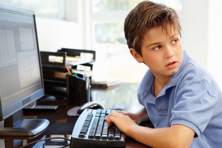 A young boy typing on a desktop computer, looking over his shoulder