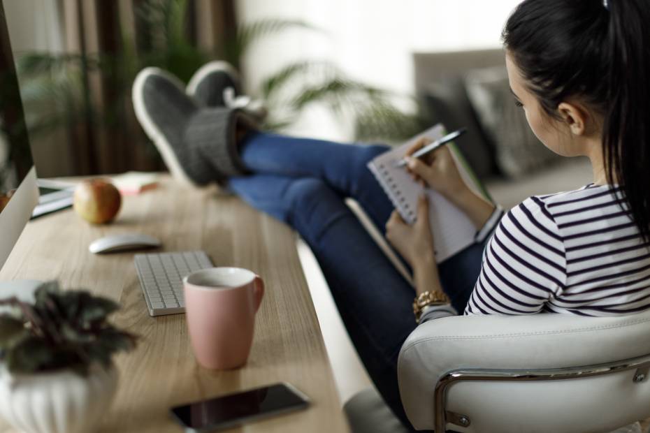 Woman facing away from the camera with her feet up on a desk and writing in a notebook.