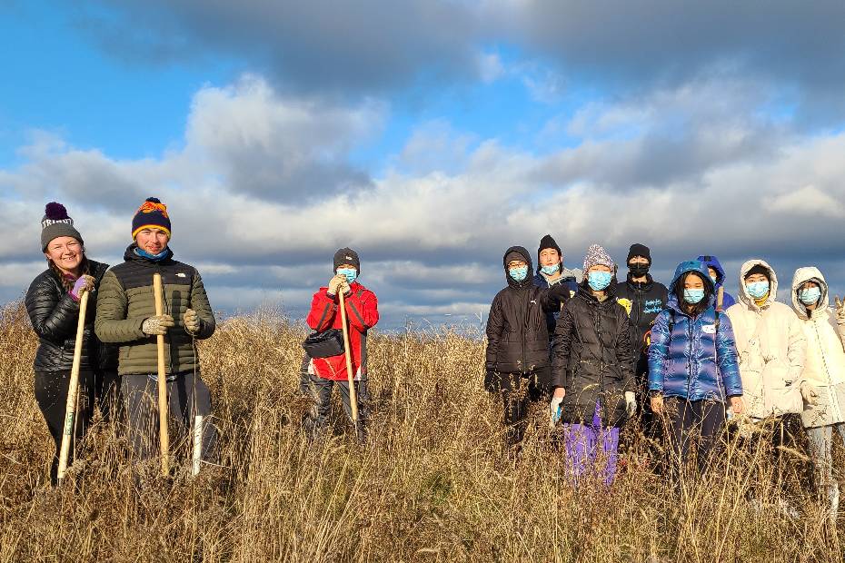 13 Green Space - Newcomer Youth Climate Forum participants, standing with tools in the high grass of a watershed area
