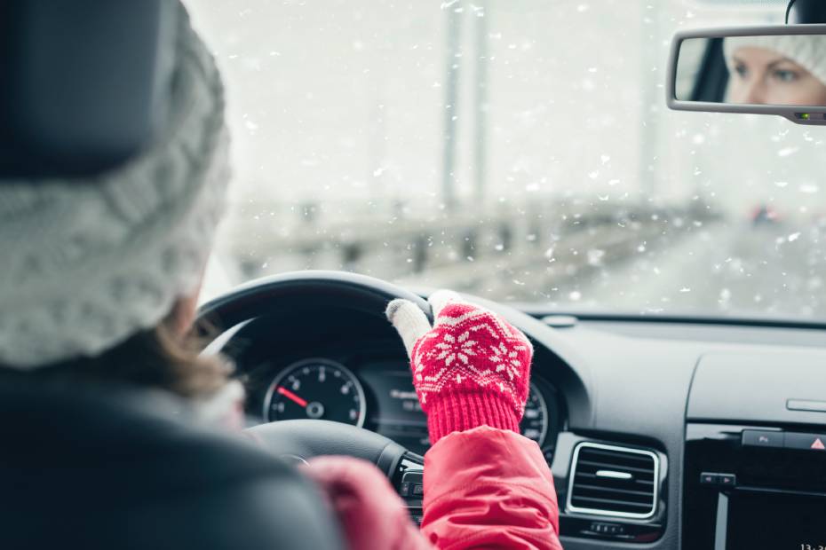 A woman wearing a wooly hat and gloves drives her EV in cold, snowy winter weather
