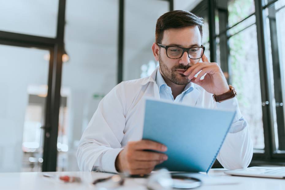 A picture showing a middle-aged physician looking in a document, in deep thoughts.