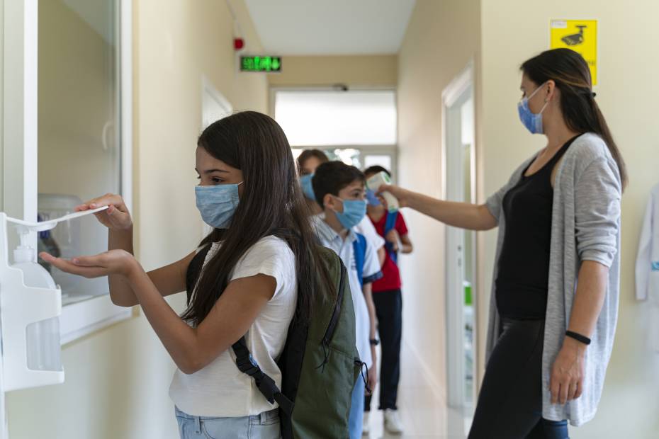 Teacher taking public health measure and checks students' temperature when they enter school