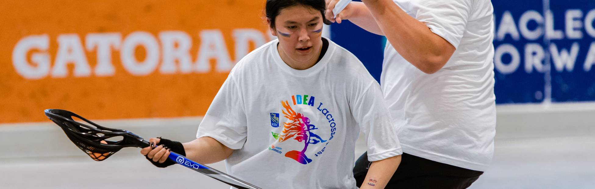 A young lacrosse player in motion, practicing with a coach on an indoor lacrosse court