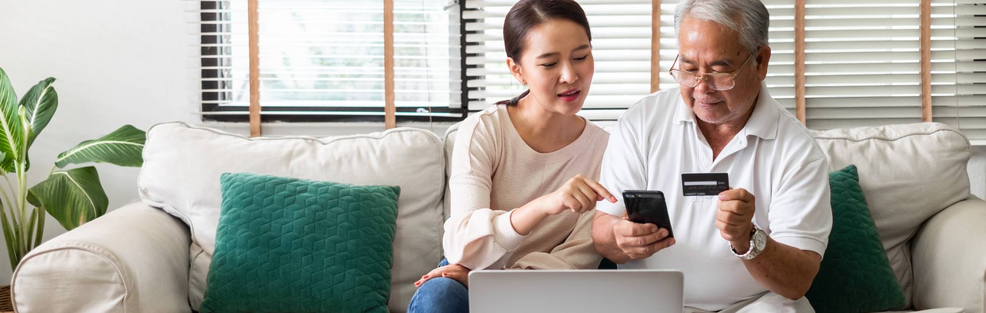 Asian woman teaching a senior to use credit card and phone for online shopping