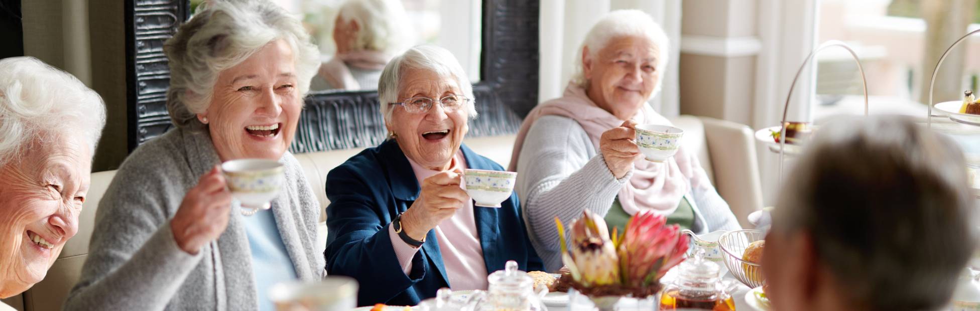 A smiling group of elderly Canadian women sitting at a table, having tea