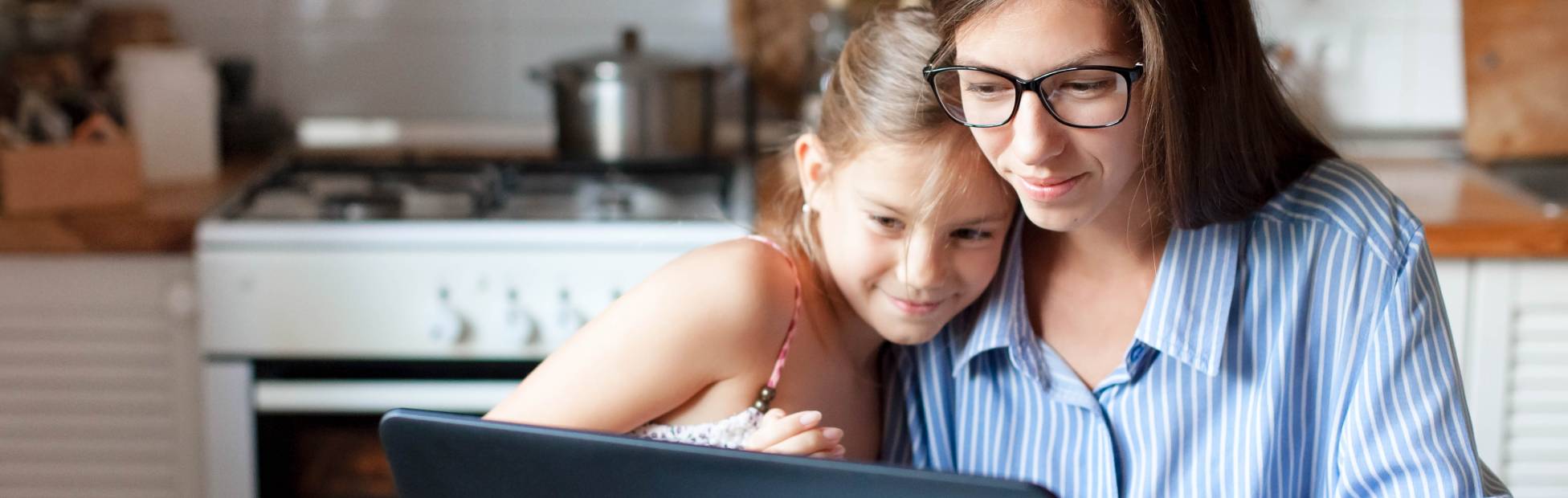 A smiling mother and daughter hugging, looking at a laptop