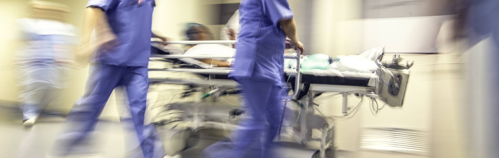 A blurred image showing a doctor and a nurse pulling hospital trolley quickly along the hospital hallway.