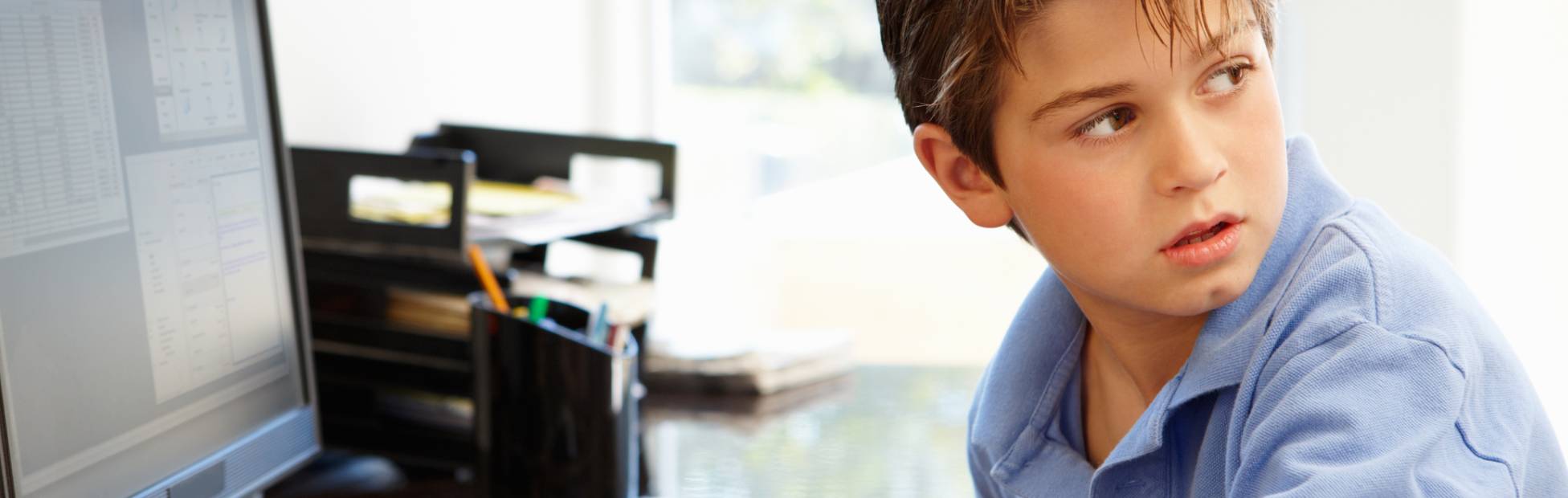 A young boy typing on a desktop computer, looking over his shoulder