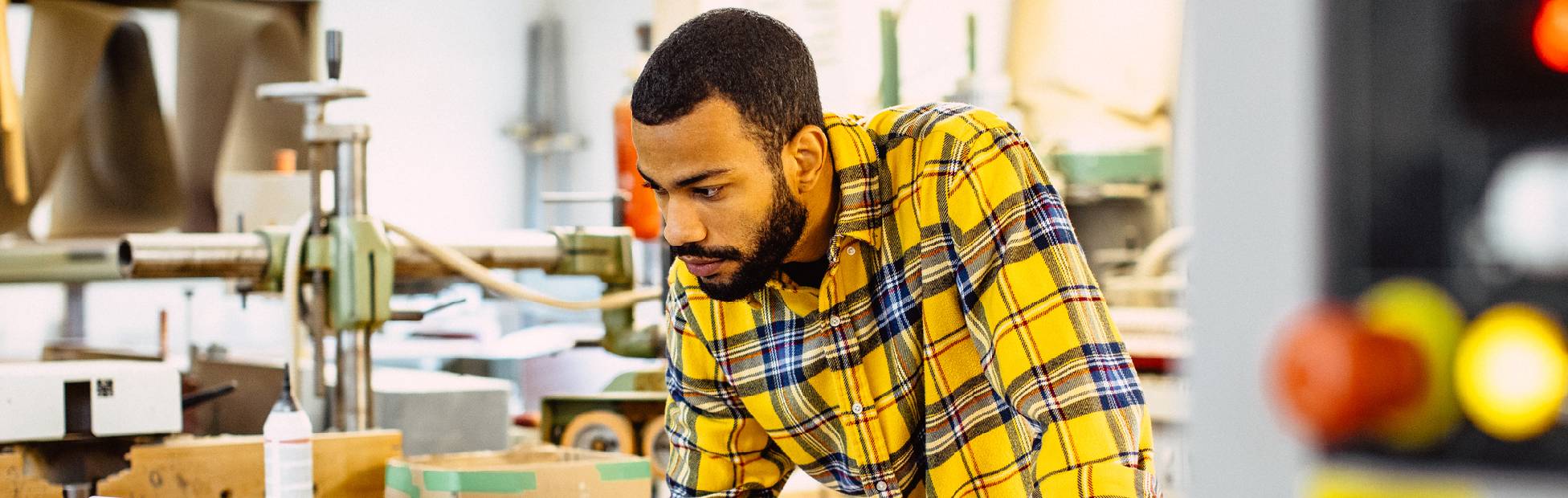 A Caribbean business owner in his machine shop, leaning over a laptop