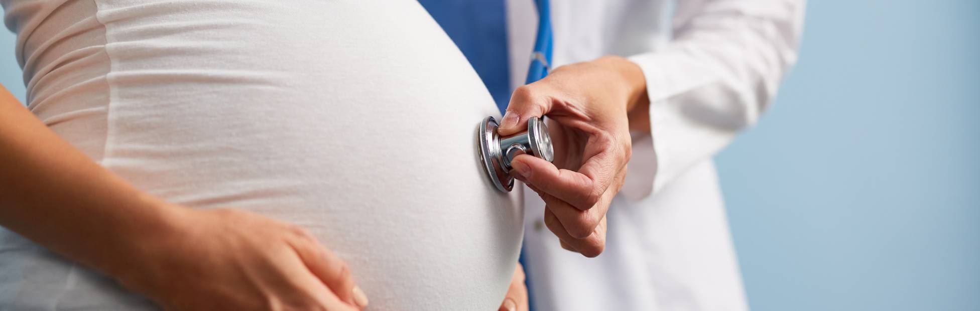 A doctor listening to the baby heart rate in pregnant female abdomen