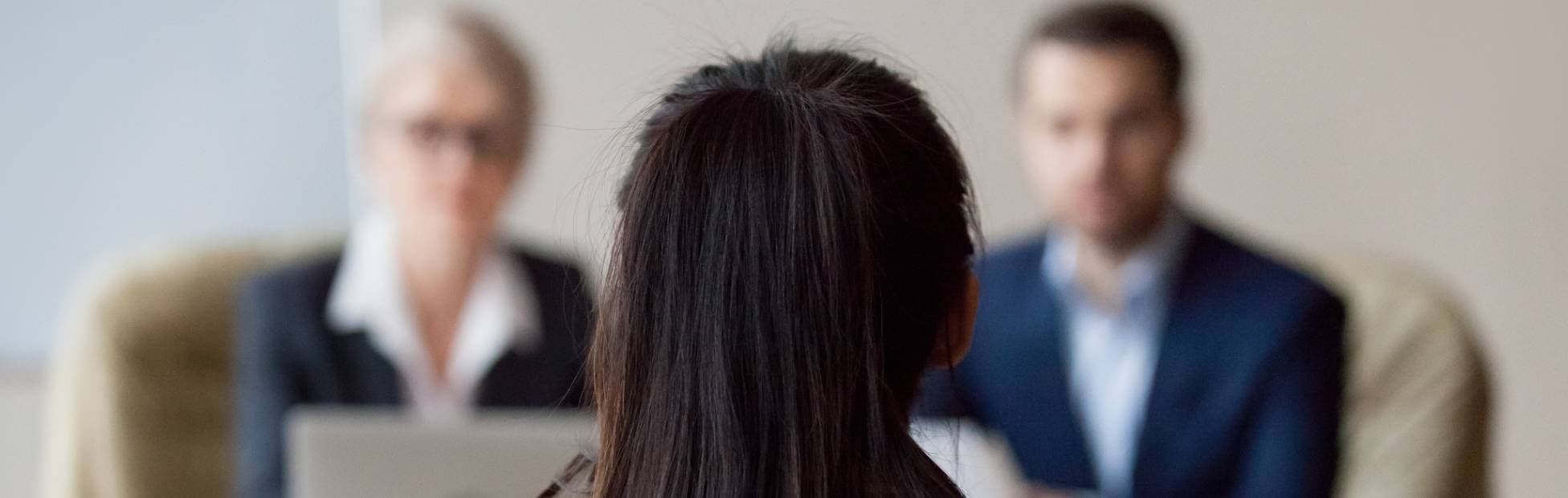 A candidate sitting with her back to the camera, being interviewed by two university professors.