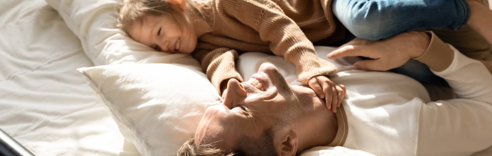 Happy father and little daughter relaxing in cozy bed together
