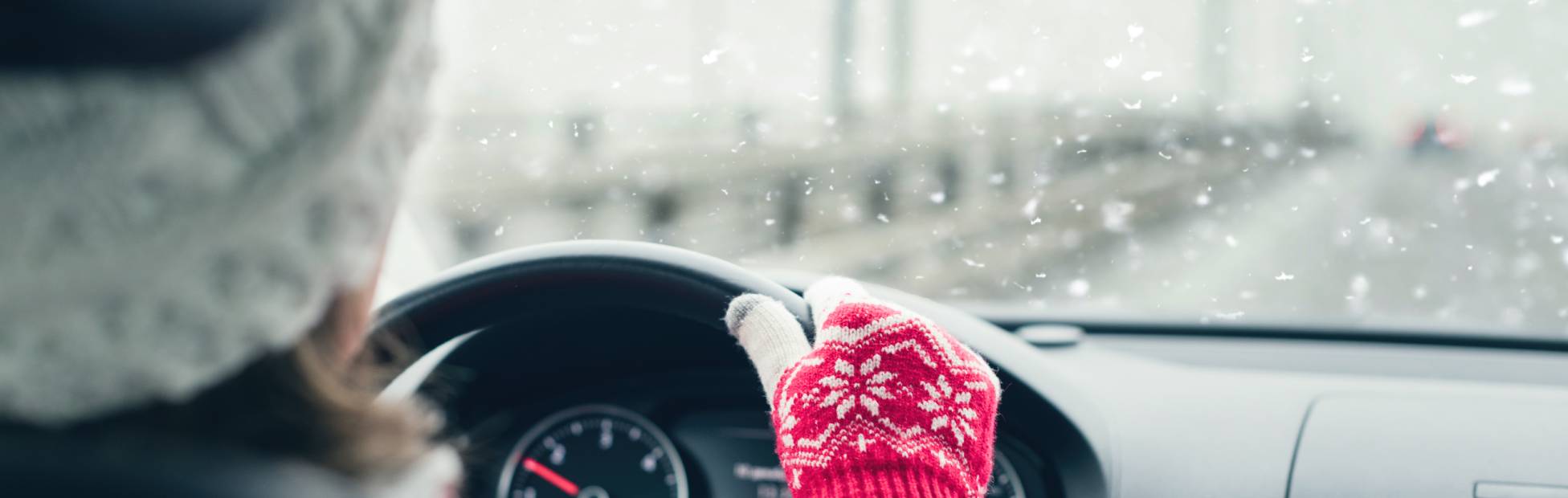 A woman wearing a wooly hat and gloves drives her EV in cold, snowy winter weather