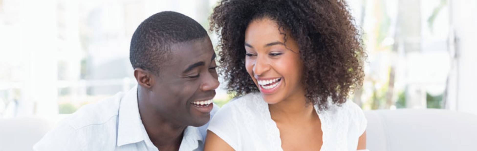 A picture showing a happy couple sitting on a sofa, laughing at something on her phone.