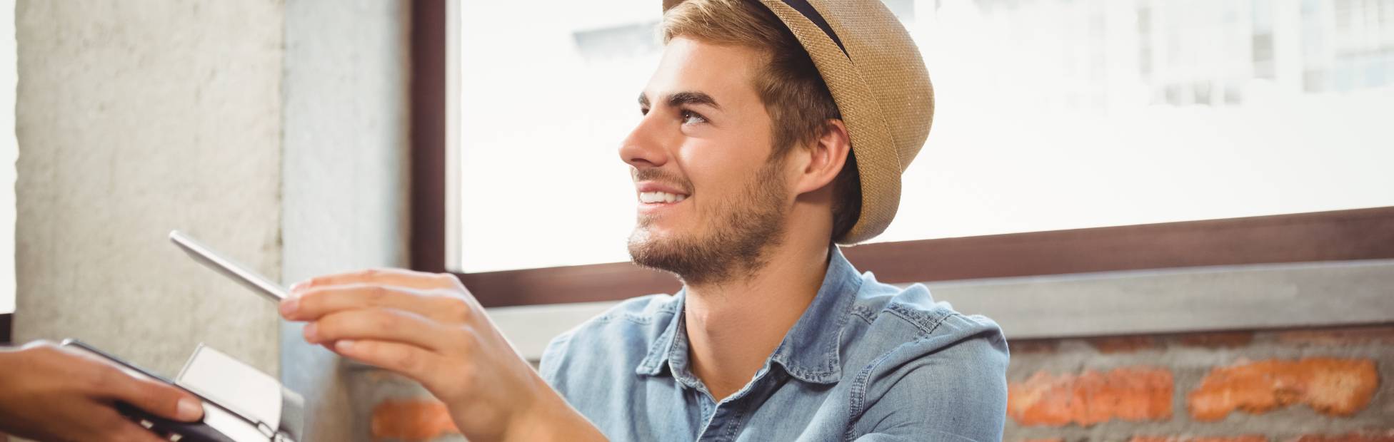 Handsome hipster student tapping to pay with his smartphone mobile device at a coffee shop