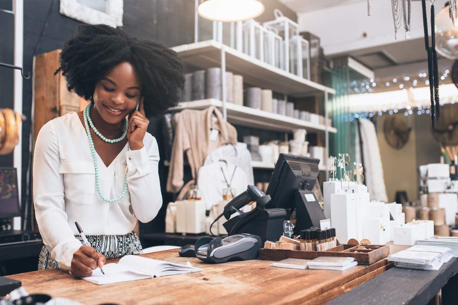 A young female Caribbean entrepreneur in her clothing and home goods store, reconnecting with customers on the phone.