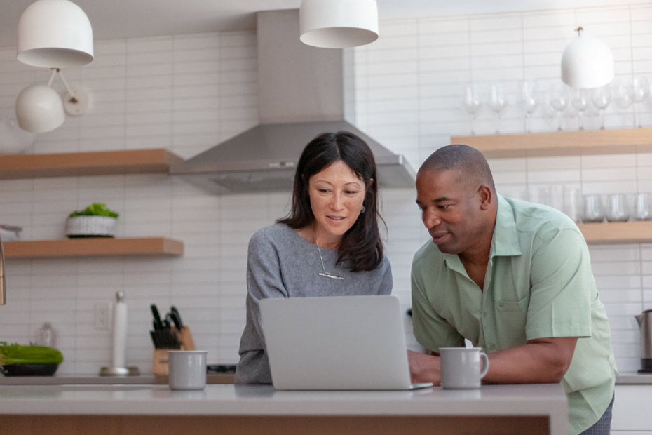 A picture showing a happy middle-aged couple looking at the laptop on their kitchen counter.
