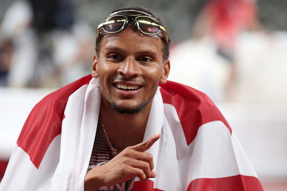 Six-time Olympic medalist and 200m champion Andre De Grasse smiling, wrapped in the Canadian flag