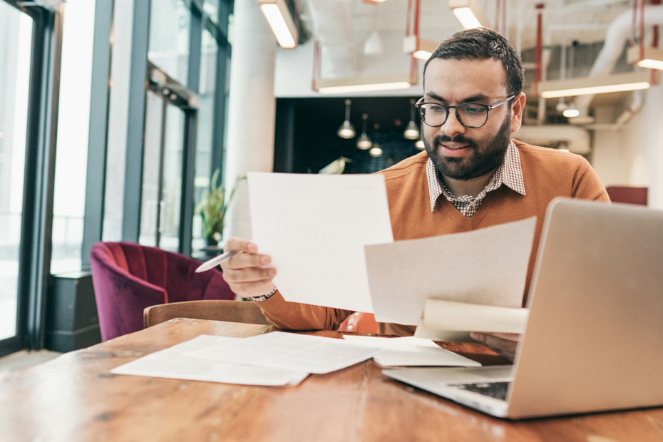 Man reviewing papers in front of laptop