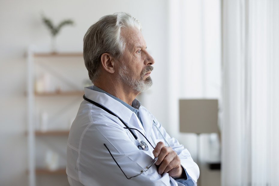 A shot of a senior doctor looking through window lost in thought.