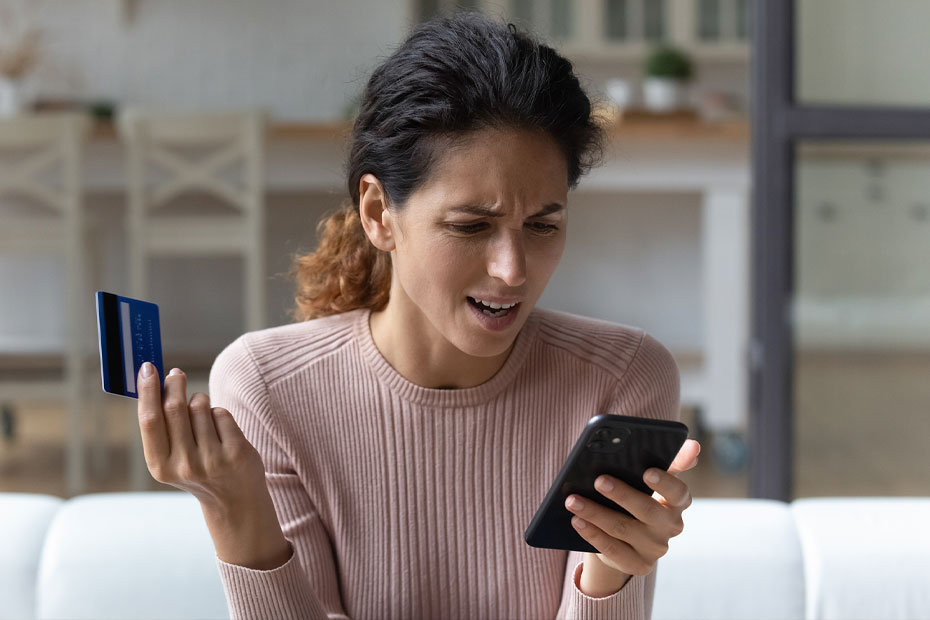 A confused lady holding her phone and credit card trying to login to her account.