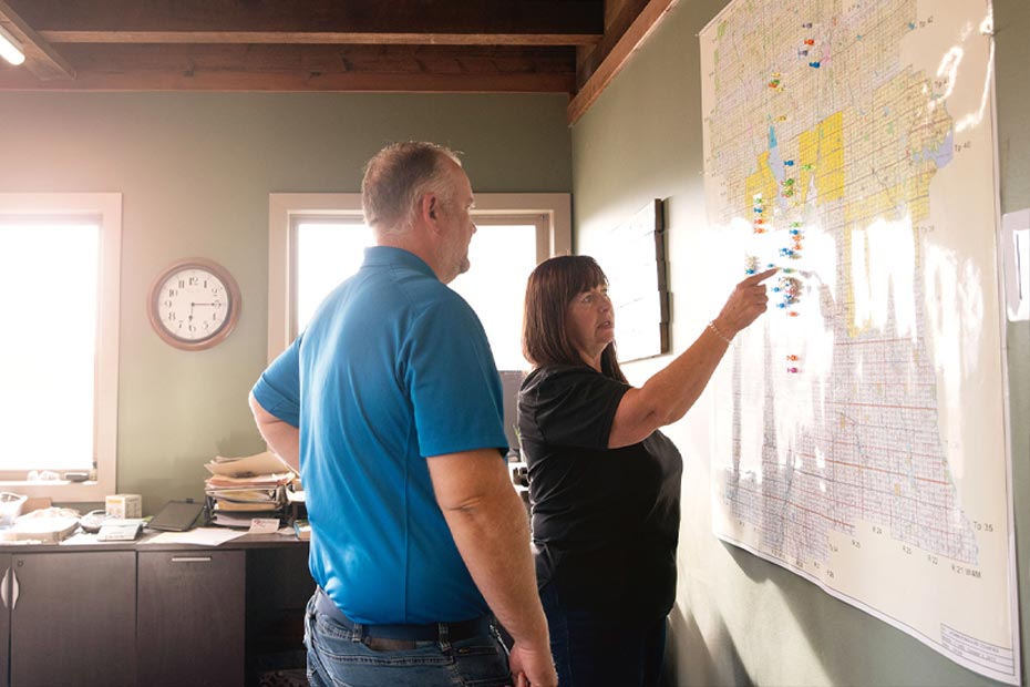 A female arm manager in her office pointing to an aerial map of the farm, discussing strategy with a male employee.