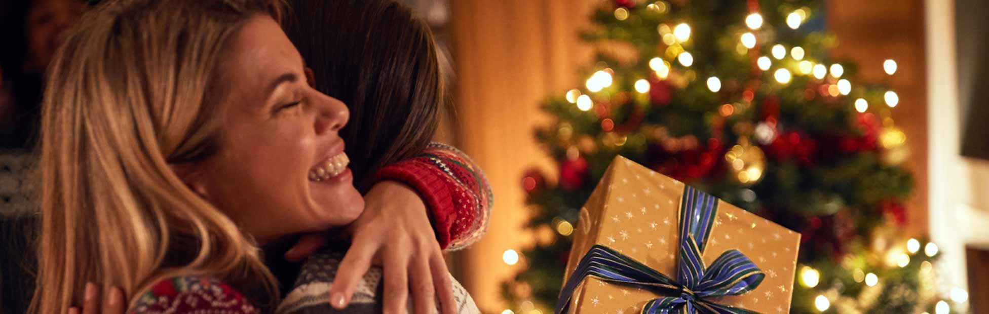 An excited young woman hugs her friend while holding a present.