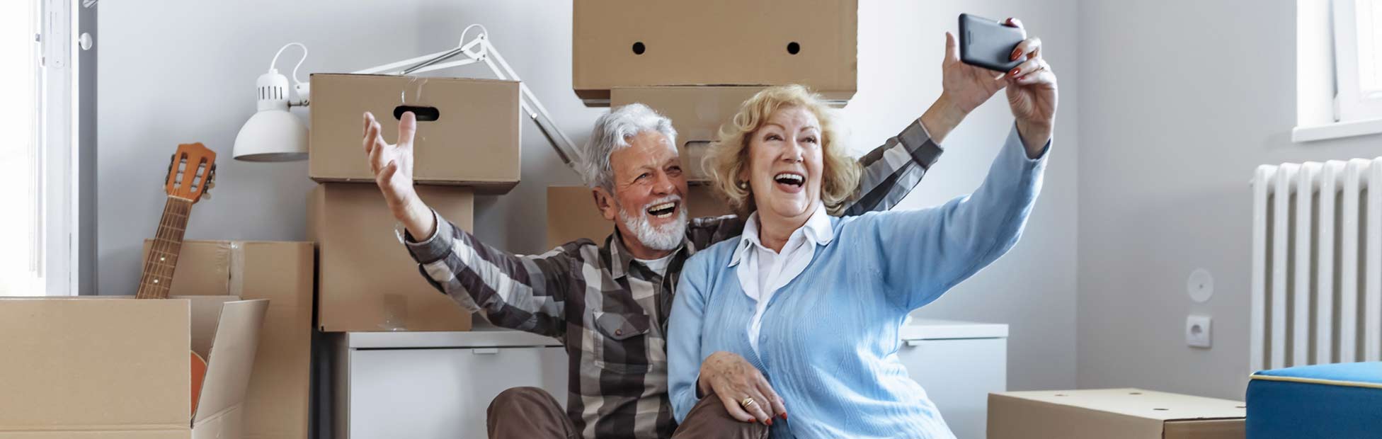 Senior couple sitting down after the move in to take a selfie.