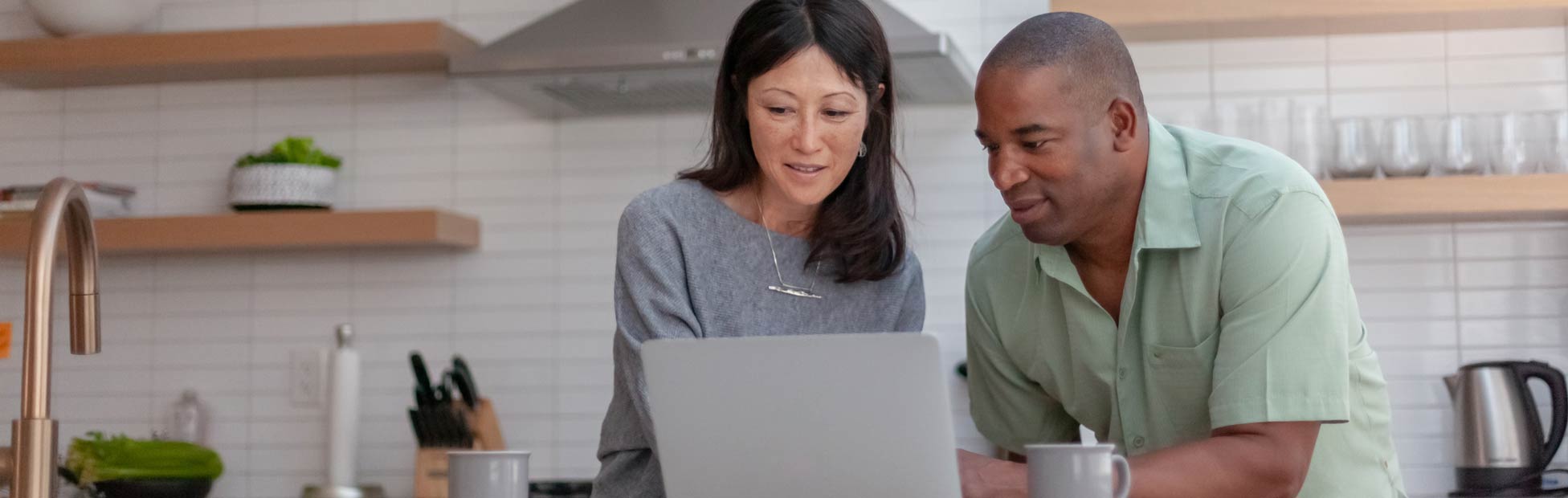 A picture showing a happy middle-aged couple looking at the laptop on their kitchen counter.