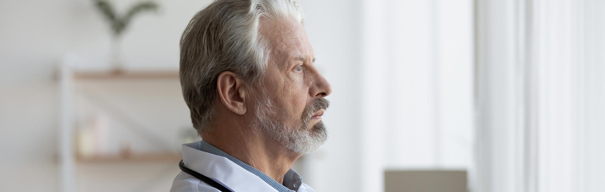 A shot of a senior doctor looking through window lost in thought.